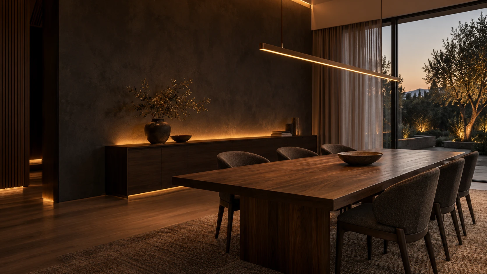 Walnut dining table, sculptural upholstered chairs and a slender glowing bronze pendant